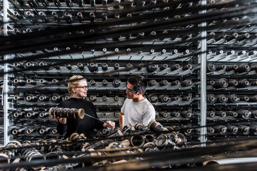 To arbejdere diskuterer blandt trådspoler i fabrik.